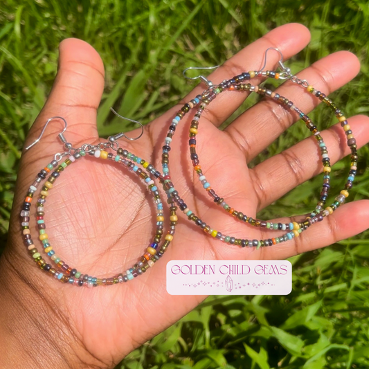 Colorful beaded hoop earrings held in a hand with a grassy background, featuring 'Golden Child Gems' branding.